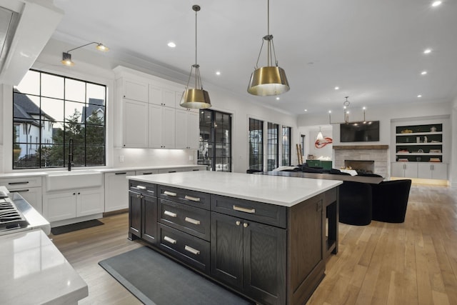 kitchen featuring white cabinetry, light wood-type flooring, a stone fireplace, a sink, and decorative light fixtures