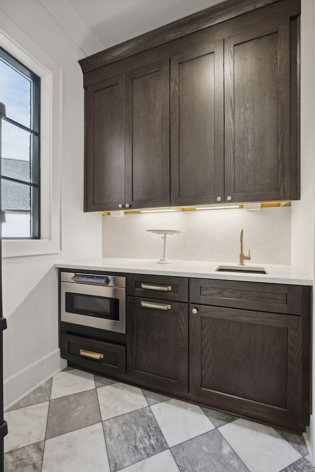 kitchen featuring a sink, dark brown cabinetry, light countertops, and baseboards