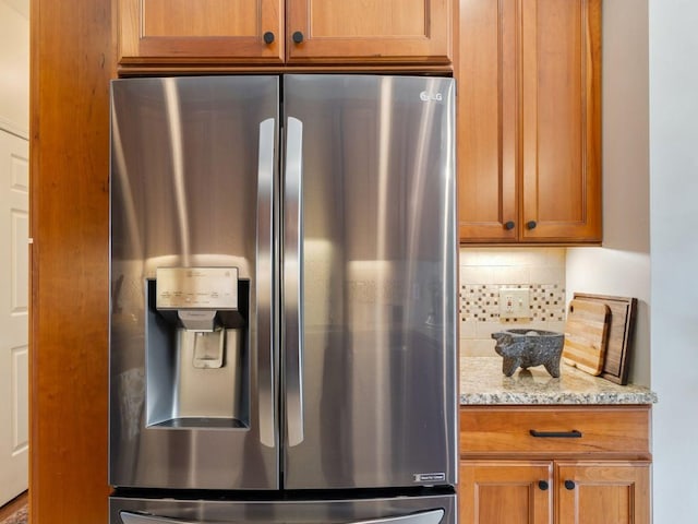 kitchen with stainless steel refrigerator with ice dispenser, tasteful backsplash, light stone countertops, and brown cabinetry