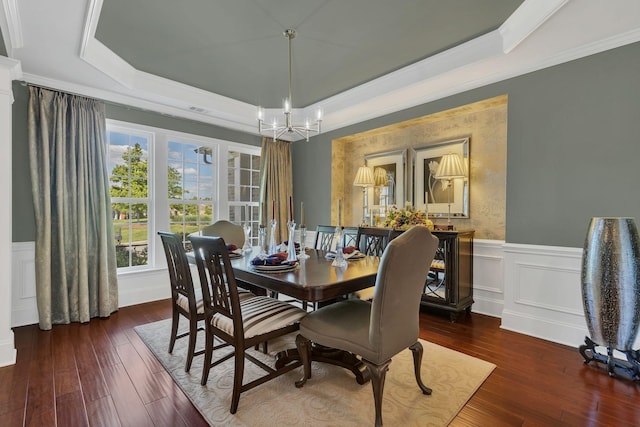 dining area featuring a raised ceiling, a chandelier, ornamental molding, wainscoting, and wood-type flooring
