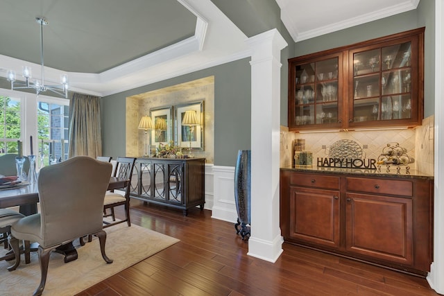 dining space with dark wood finished floors, decorative columns, a chandelier, crown molding, and a wainscoted wall