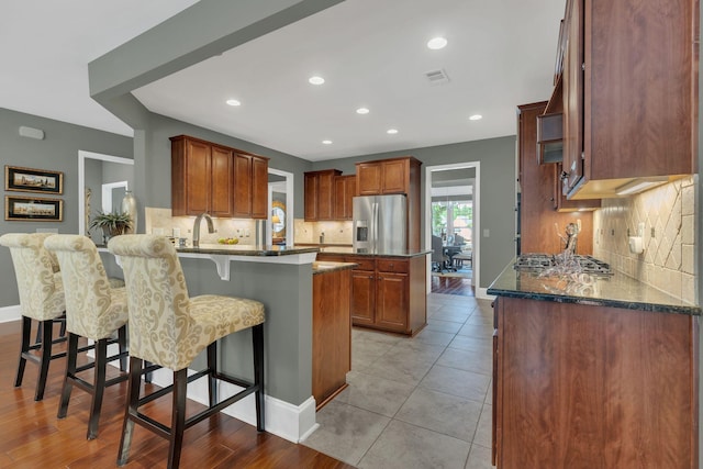 kitchen with stainless steel fridge with ice dispenser, a peninsula, tasteful backsplash, a breakfast bar, and recessed lighting