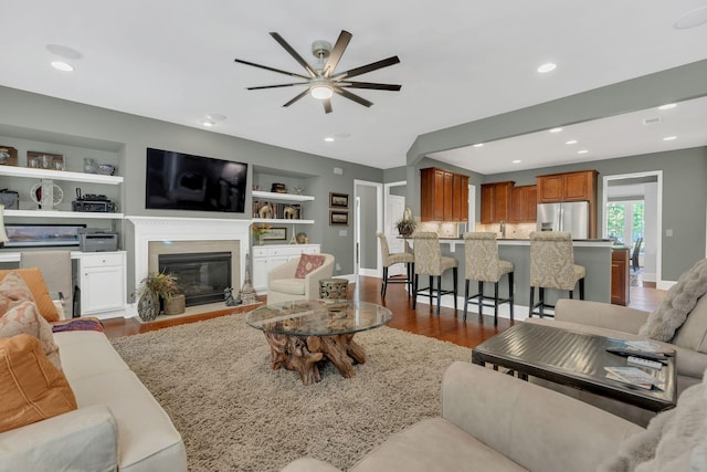 living area featuring dark wood-style flooring, ceiling fan, a fireplace with flush hearth, recessed lighting, and built in features