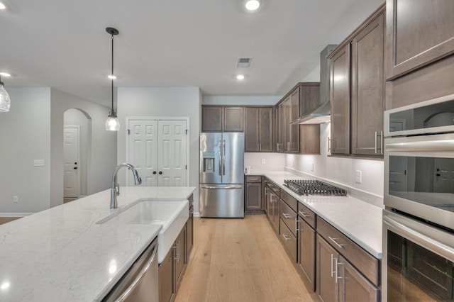 kitchen with appliances with stainless steel finishes, light wood-style floors, light stone countertops, arched walkways, and a sink