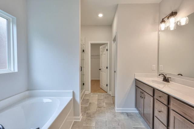 bathroom featuring a garden tub, vanity, a walk in closet, baseboards, and recessed lighting