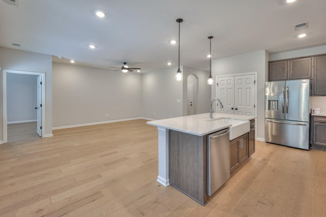 kitchen featuring appliances with stainless steel finishes, a sink, a ceiling fan, light wood finished floors, and baseboards