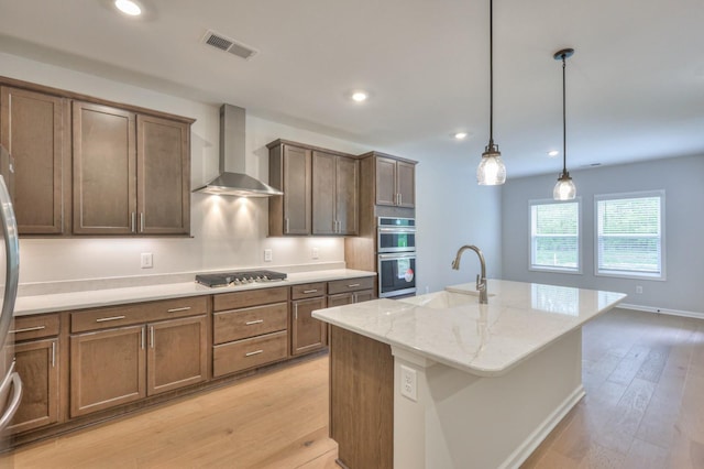 kitchen featuring wall chimney range hood, a sink, appliances with stainless steel finishes, light wood-style floors, and recessed lighting