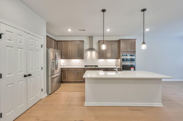 kitchen with appliances with stainless steel finishes, wall chimney range hood, a sink, light wood-type flooring, and recessed lighting