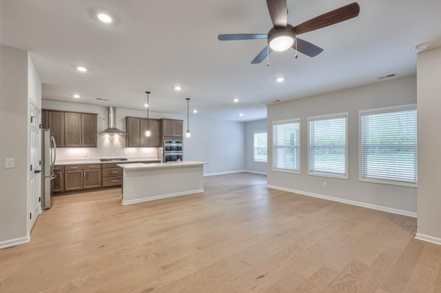 kitchen featuring wall chimney exhaust hood, appliances with stainless steel finishes, open floor plan, light wood finished floors, and baseboards