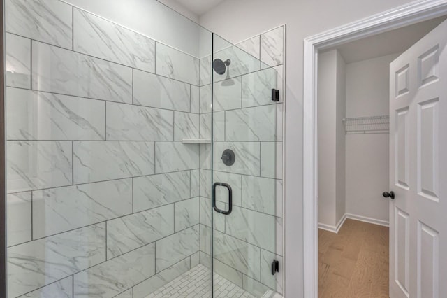 bathroom with a stall shower, wood finished floors, a walk in closet, and baseboards