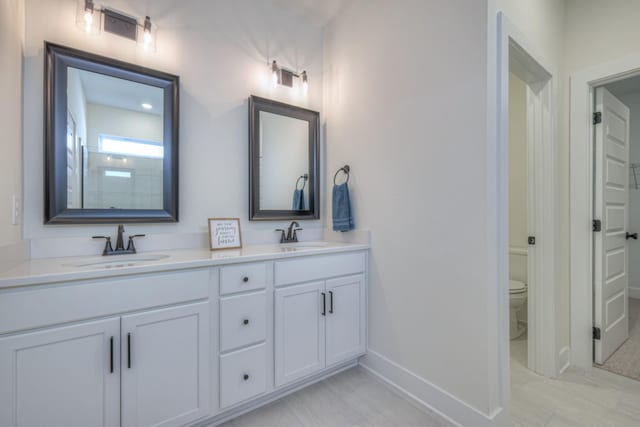 bathroom with baseboards, double vanity, and toilet