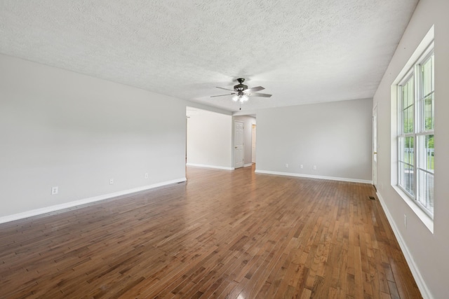 empty room with a textured ceiling, ceiling fan, wood finished floors, and baseboards