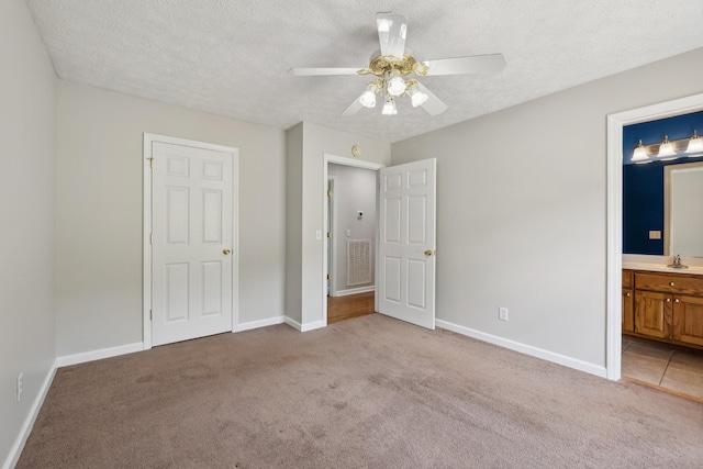 unfurnished bedroom with a sink, light carpet, a textured ceiling, baseboards, and ensuite bath