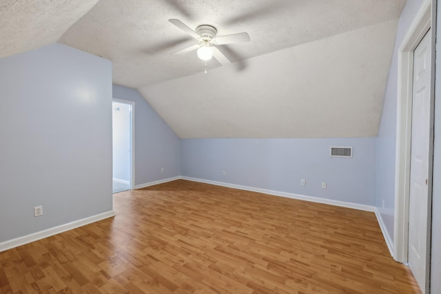 additional living space with light wood-type flooring, ceiling fan, vaulted ceiling, a textured ceiling, and baseboards