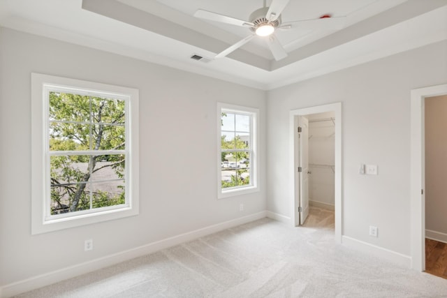 unfurnished bedroom with a tray ceiling, a walk in closet, baseboards, light carpet, and a ceiling fan
