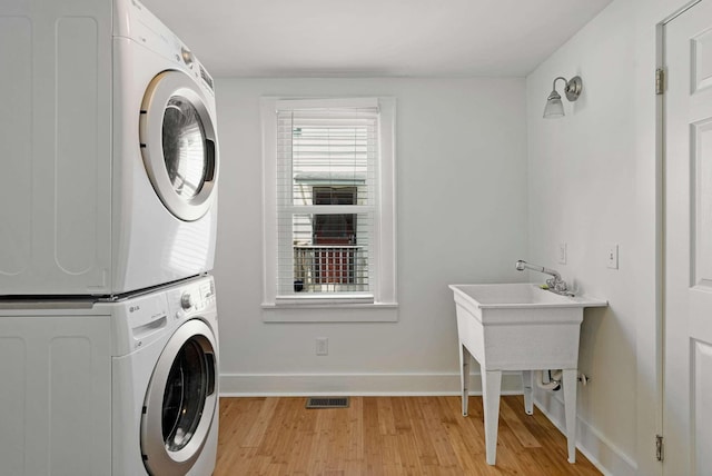 clothes washing area featuring stacked washer and clothes dryer, light wood-style floors, and baseboards