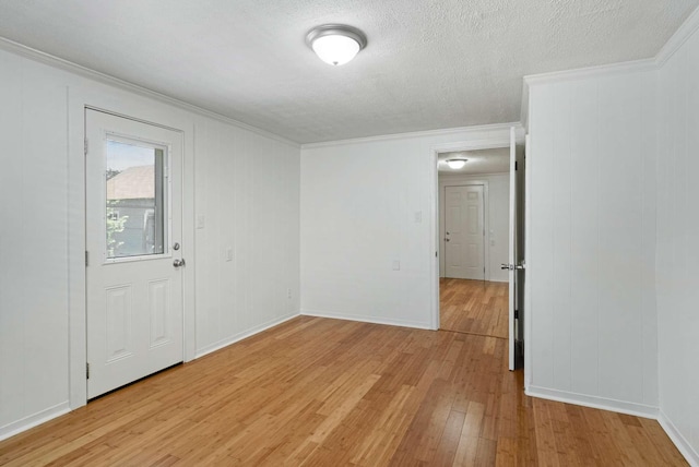 spare room with light wood-style floors, ornamental molding, a textured ceiling, and baseboards