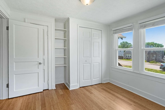 unfurnished bedroom with light wood finished floors, crown molding, a closet, a textured ceiling, and baseboards