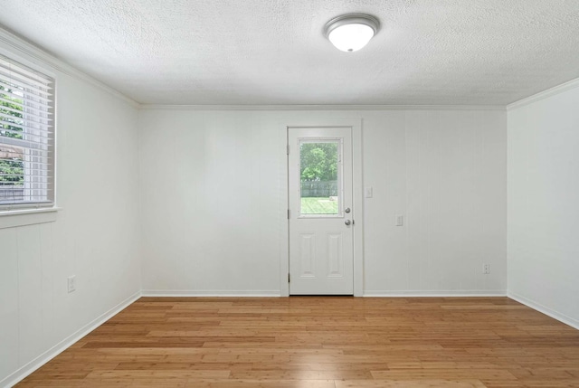empty room with a textured ceiling, light wood-style floors, ornamental molding, and baseboards