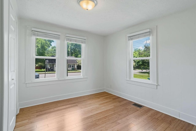 empty room featuring light wood finished floors, a textured ceiling, healthy amount of natural light, and baseboards