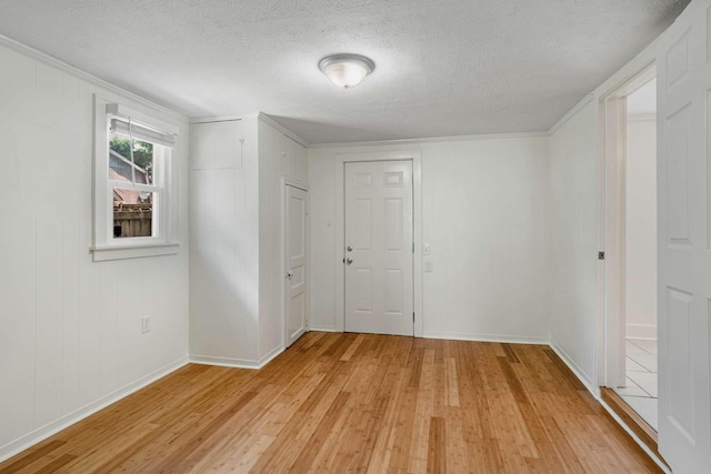 spare room with light wood finished floors, a textured ceiling, ornamental molding, and baseboards