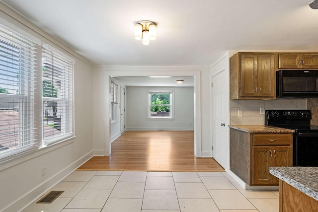 kitchen featuring black appliances, brown cabinets, light wood-type flooring, backsplash, and baseboards