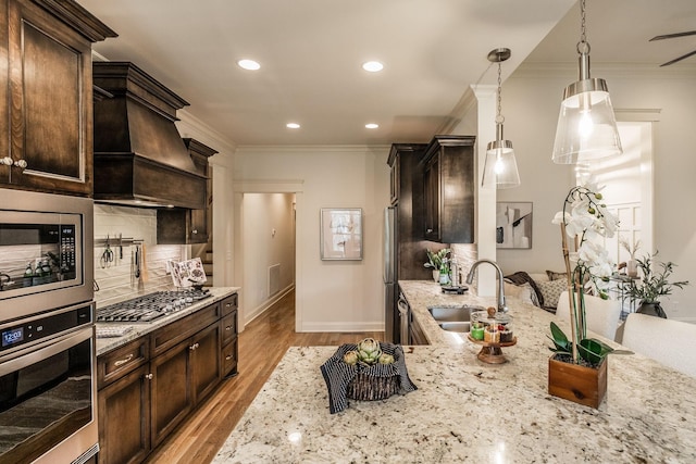 1219 Ben Forkum Dr, Lebanon, TN 37087 - kitchen featuring stainless steel appliances, a sink, light stone counters, dark brown cabinetry, and crown molding