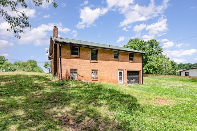 rear view of property with a chimney, brick siding, an attached garage, metal roof, and a lawn