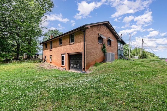 rear view of house with a garage, central AC unit, a lawn, brick siding, and a chimney