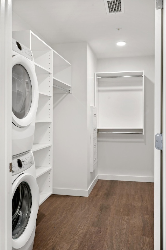 clothes washing area with stacked washer and clothes dryer, dark wood-style floors, and baseboards