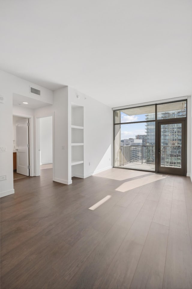 unfurnished living room featuring built in features, baseboards, and wood finished floors