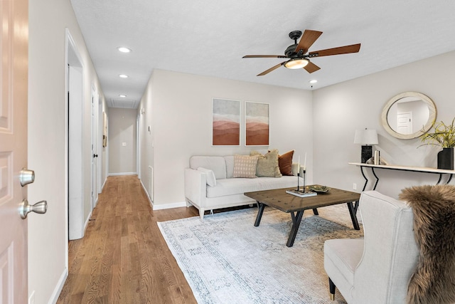 living room featuring light wood-type flooring, ceiling fan, baseboards, recessed lighting, and attic access