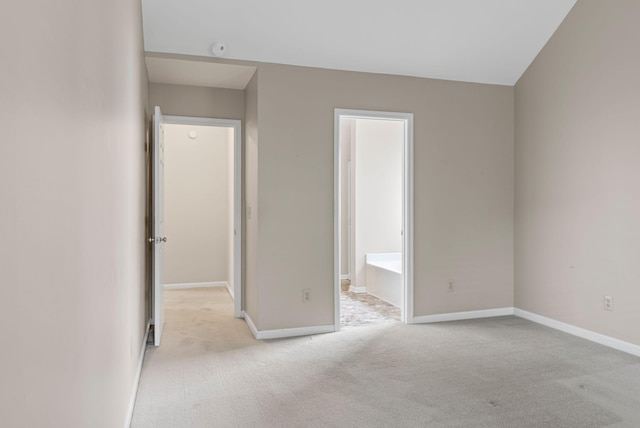 unfurnished bedroom featuring light carpet, baseboards, and ensuite bath