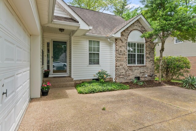 view of exterior entry featuring a shingled roof, brick siding, and crawl space