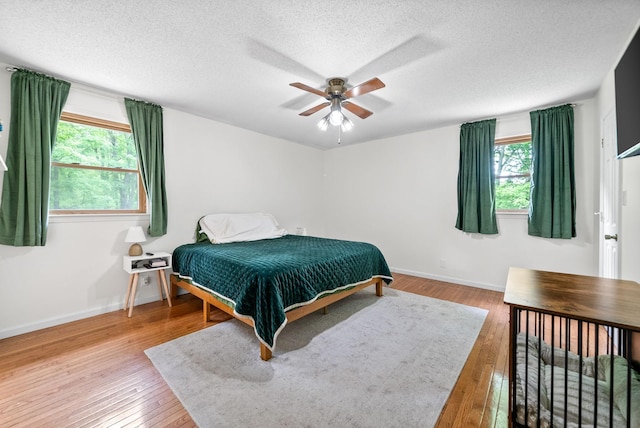 bedroom featuring multiple windows, wood-type flooring, baseboards, a textured ceiling, and a ceiling fan