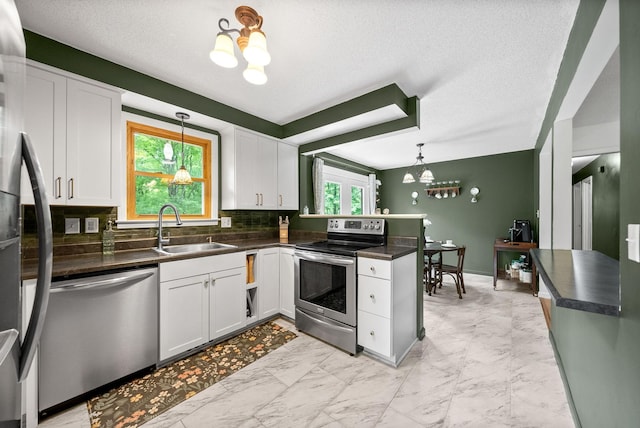 kitchen featuring stainless steel appliances, a sink, a chandelier, dark countertops, and a peninsula