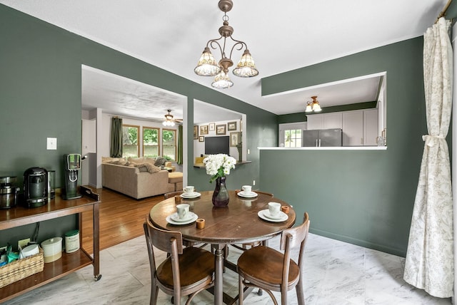 dining room with healthy amount of natural light, ceiling fan, a chandelier, and light marble finish flooring