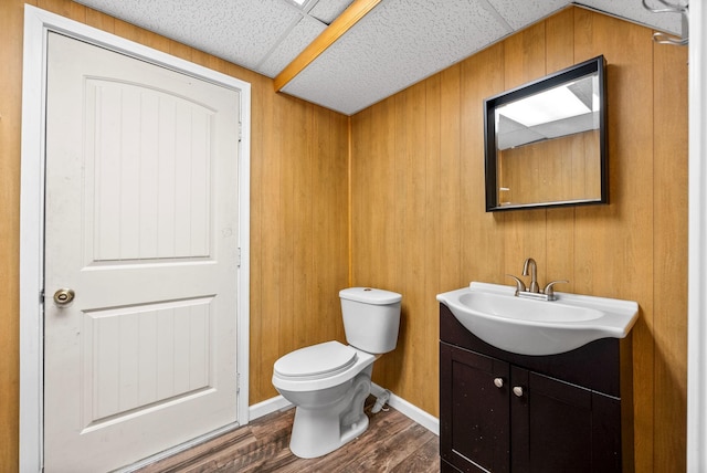 half bath featuring toilet, vanity, wood finished floors, wood walls, and baseboards