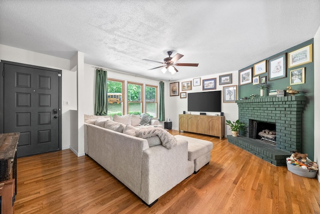living room featuring wood finished floors, ceiling fan, a fireplace, a textured ceiling, and baseboards