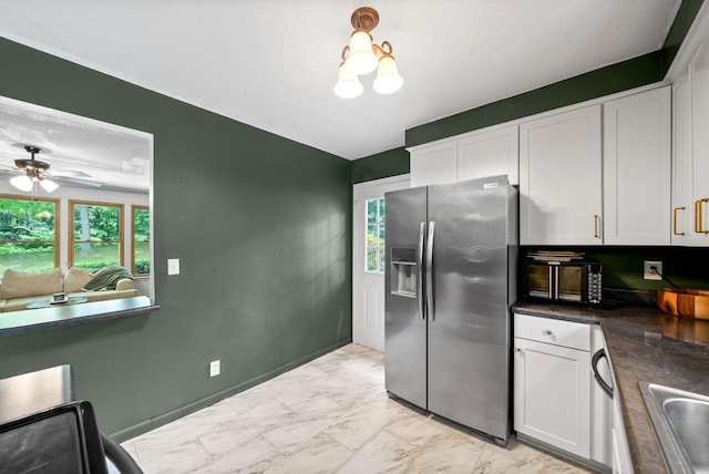 kitchen with stainless steel fridge, light marble finish floors, white cabinets, dark countertops, and plenty of natural light