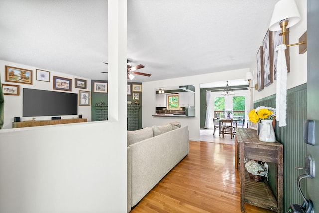 living room featuring light wood-type flooring, ceiling fan, a textured ceiling, and a chandelier