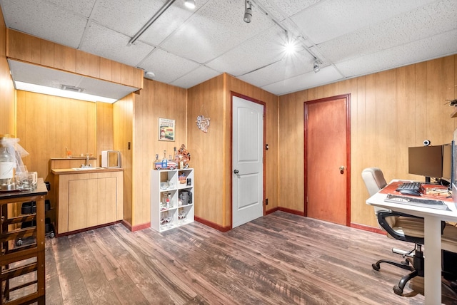 office space with a sink, wood finished floors, track lighting, wood walls, and baseboards
