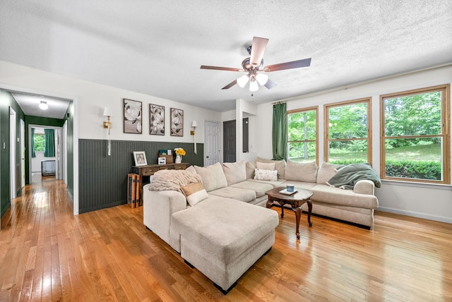 living area with light wood-style flooring, ceiling fan, baseboards, and a textured ceiling