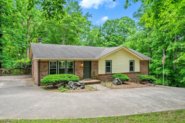 ranch-style house with brick siding, driveway, roof with shingles, and a chimney