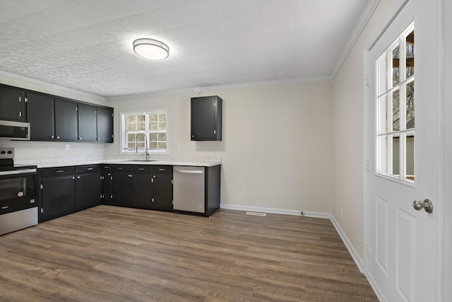 kitchen featuring appliances with stainless steel finishes, a sink, dark cabinets, crown molding, and light countertops