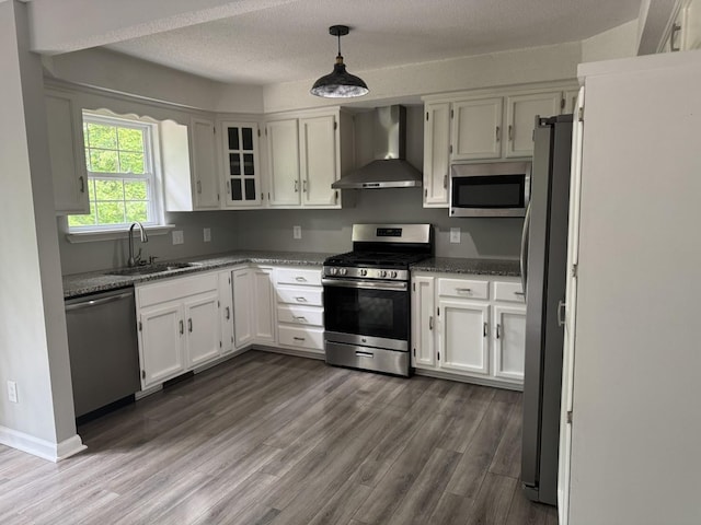 kitchen featuring wall chimney exhaust hood, appliances with stainless steel finishes, a sink, white cabinetry, and dark wood finished floors