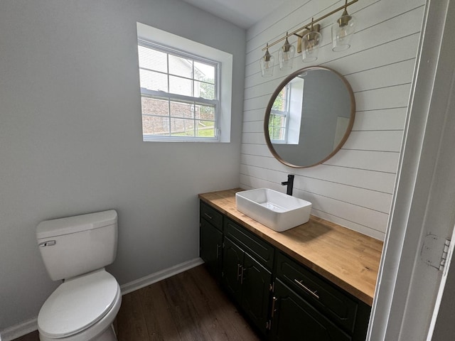 half bathroom with wood finished floors, vanity, toilet, and baseboards