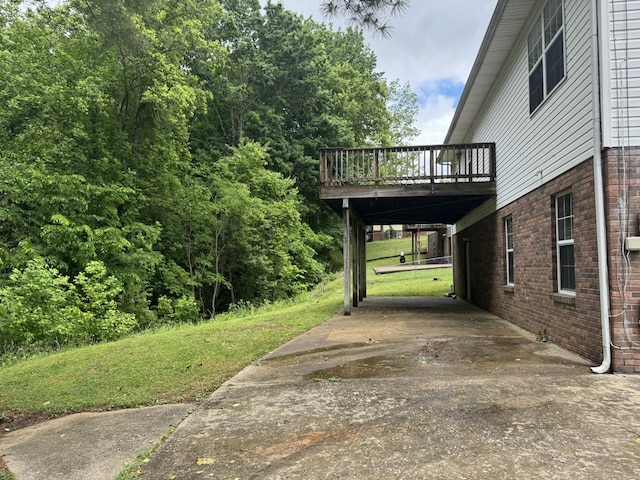 view of property exterior featuring a deck, brick siding, a lawn, concrete driveway, and a carport
