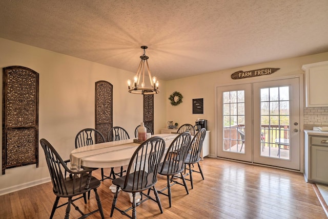 dining room with a chandelier, light wood-style flooring, a textured ceiling, and baseboards