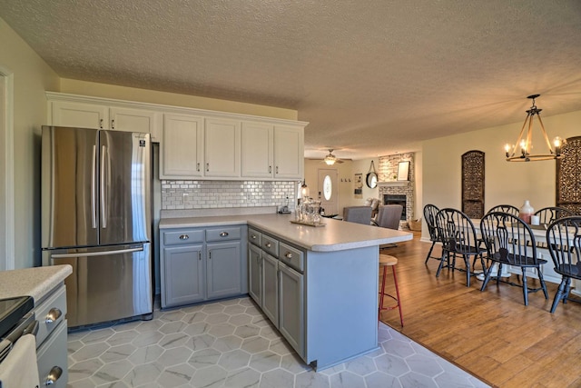 kitchen featuring stainless steel appliances, a peninsula, a fireplace, light countertops, and white cabinets